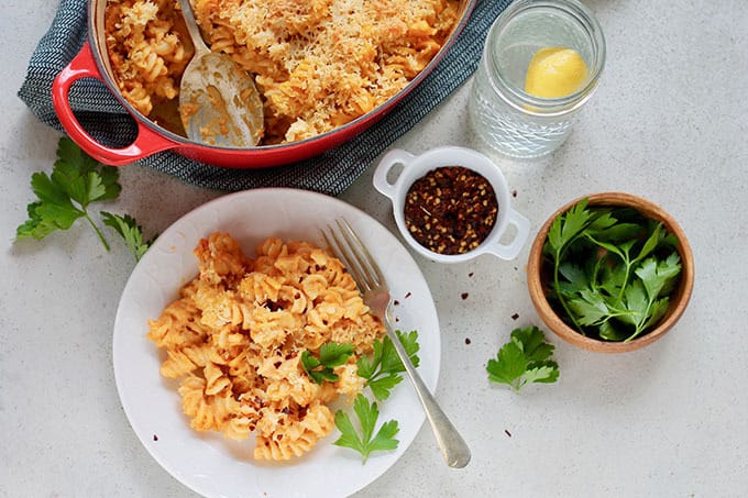 a plate of pumpkin mac and cheese with a casserole dish and spices in the background