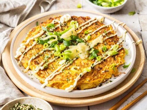 Okonomiyaki (Japanese cabbage pancake) topped with mayo, pickled ginger, and scallions on a white plate