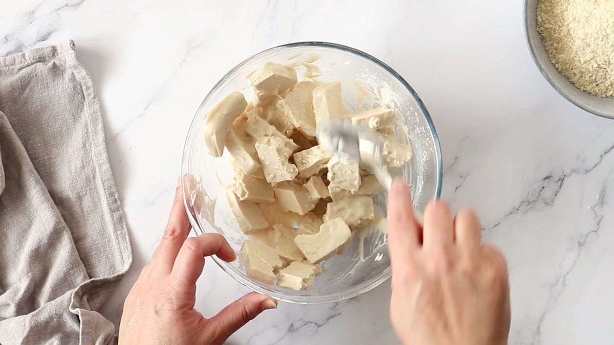 Chunks of tofu being stirred into batter to coat them.