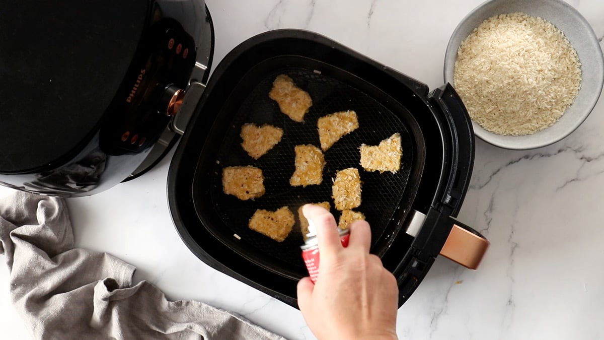 Overhead photo of tofu nuggets being sprayed with oil in an air fryer basket
