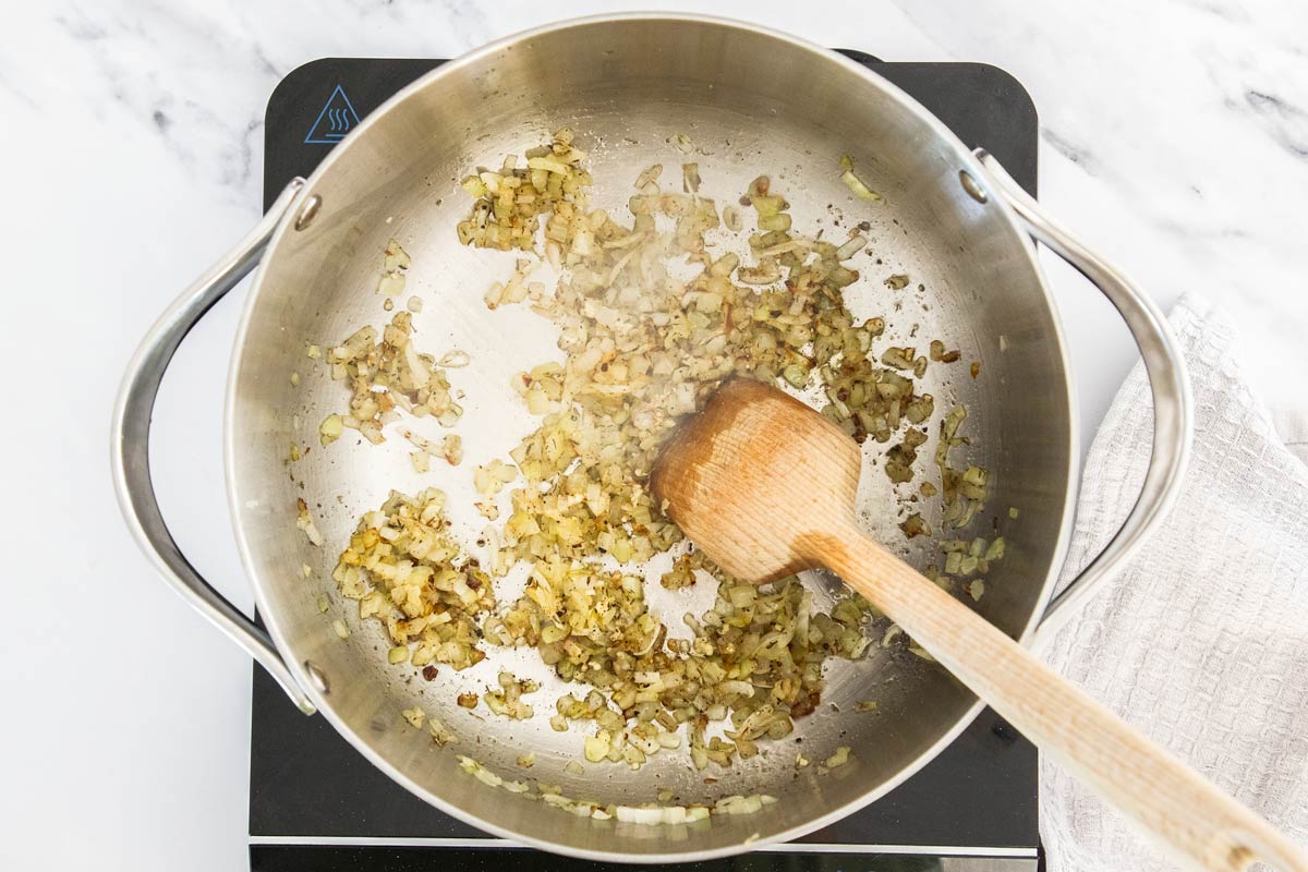 Overhead photo of onions being sautéd in a stanless steel saucepan.