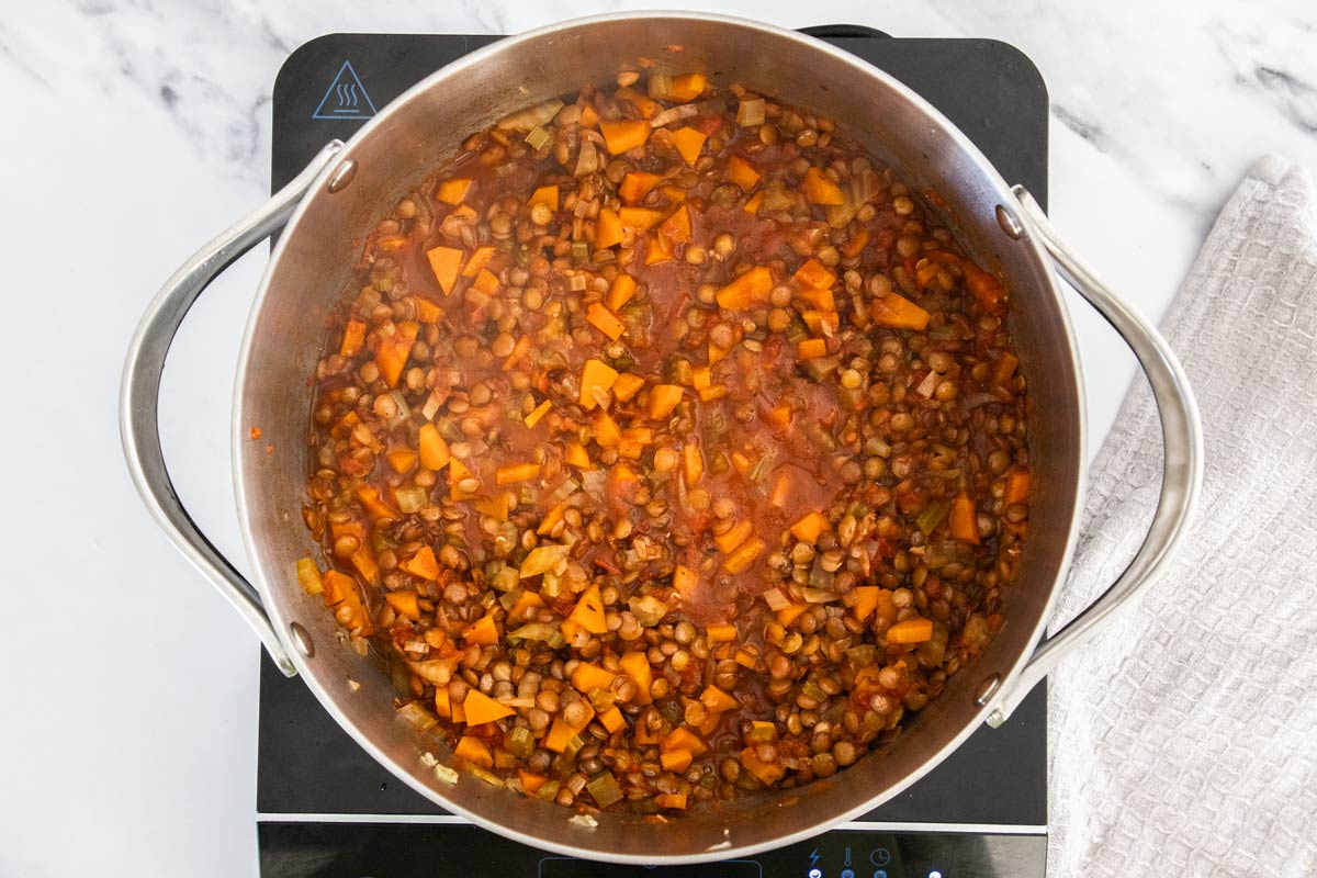 Lentil shepherd's pie filling simmering in a stainless steel saucepan.