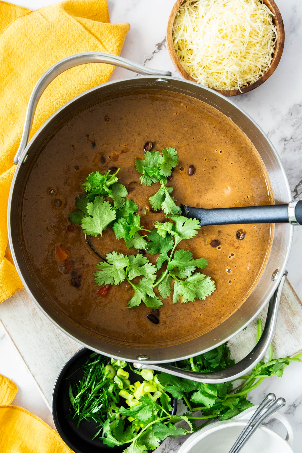 Overhead photo of vegetarian black bean soup in a stainless steel soup pot with a black ladle inside.