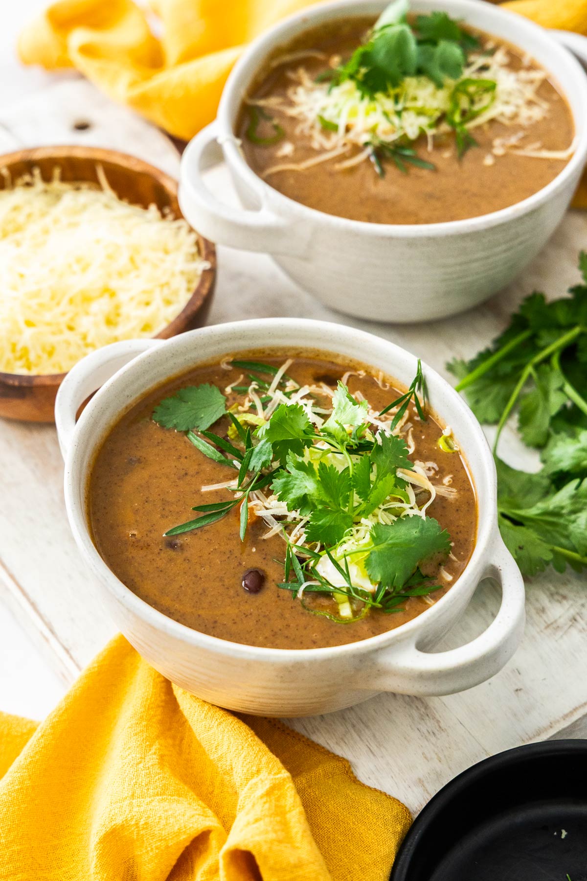 Two white bowls of black bean soup topped with cilantro and shredded cheese.