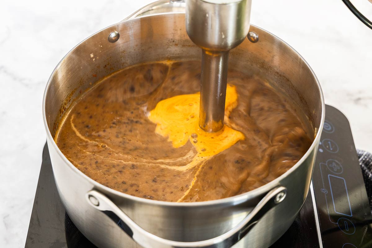Black bean soup being blended in a soup pot using an immersion blender.