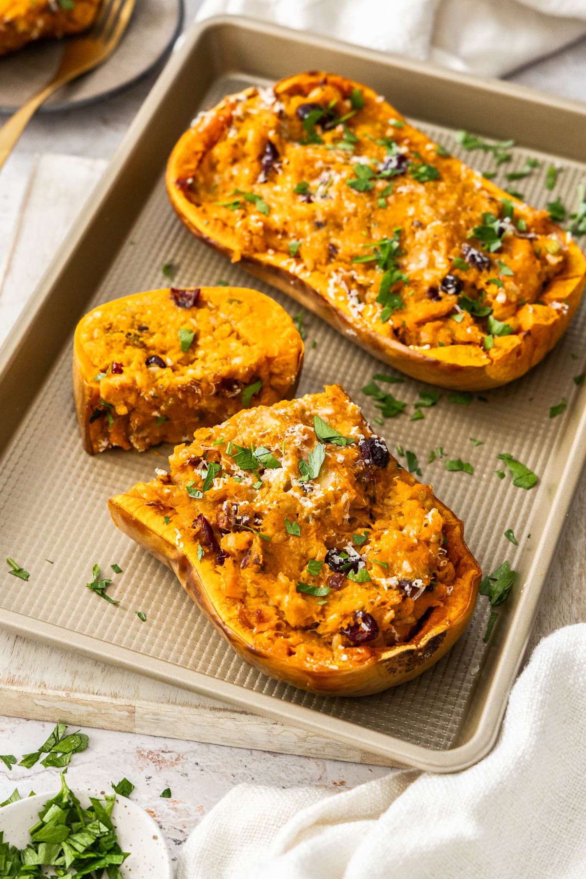 Two stuffed butternut squash halves on a baking sheet sprinkled with fresh parsley.
