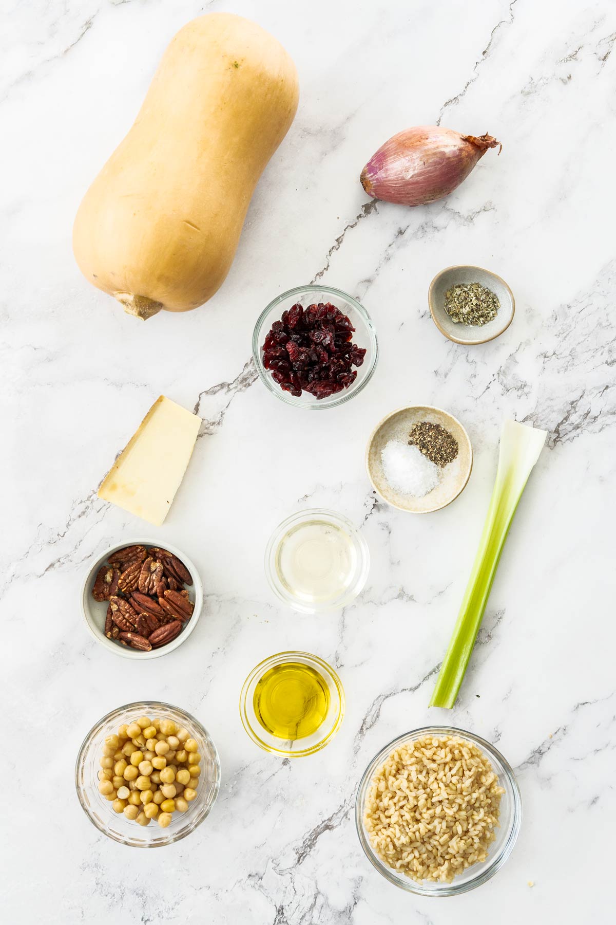 Butternut squash, shallot, celery, brown rice, white wine, dried cranberries, pecans, and cheese on a marble background.