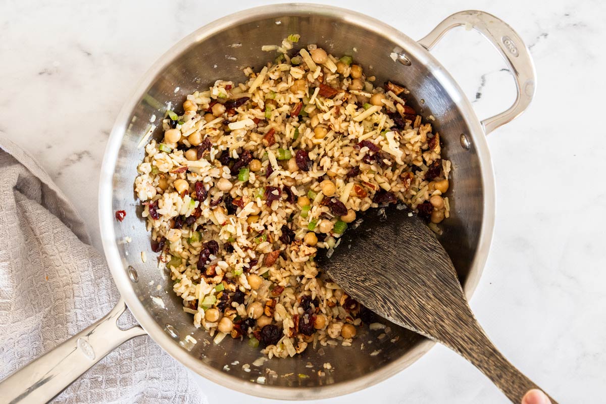 Overhead photo of brown rice stuffing be stirred together in a stainless steel pan
