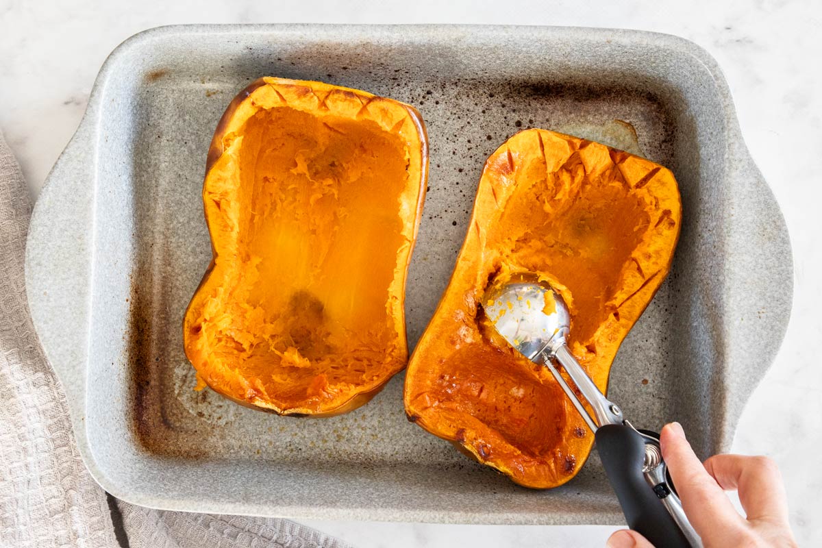 Two roasted butternut squash house with the flesh be scooped out with an ice cream scoop.