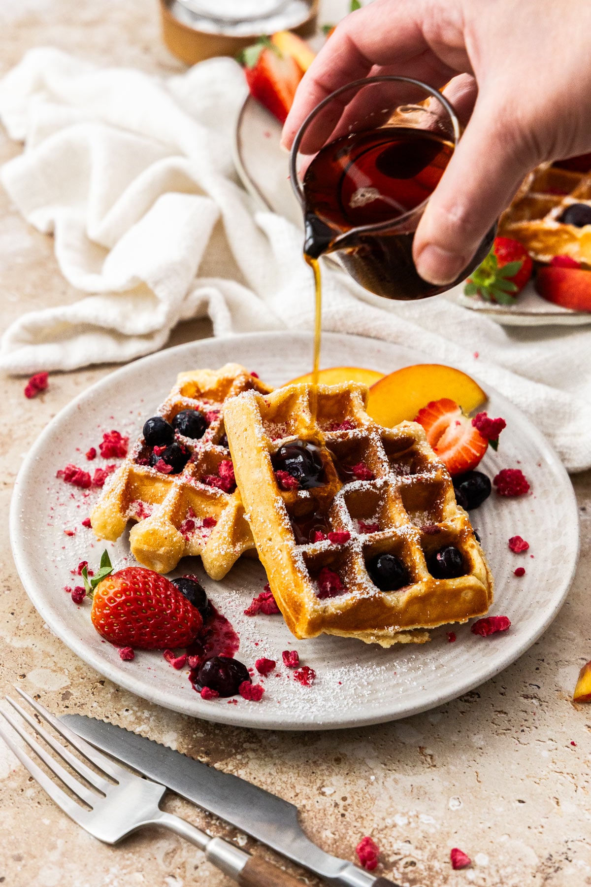 Maple syrup being poured onto two cottage cheese waffles on a white plate.