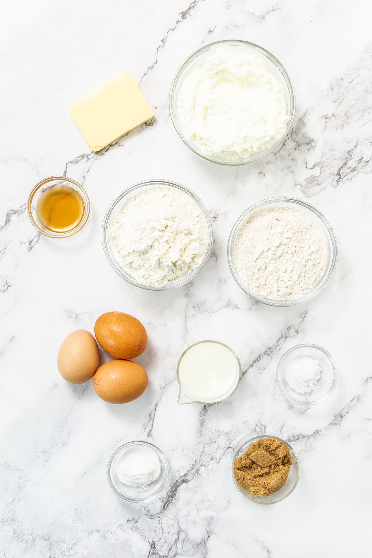 Cottage cheese, eggs, milk, melted butter, brown sugar, flour, baking powder, and salt on a marble background