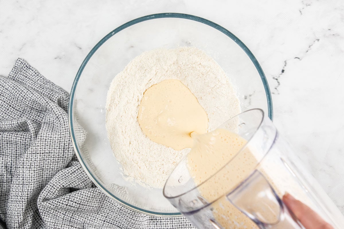 Wet ingredients for cottage cheese and waffles are being poured into a glass bowl of dry ingredients.