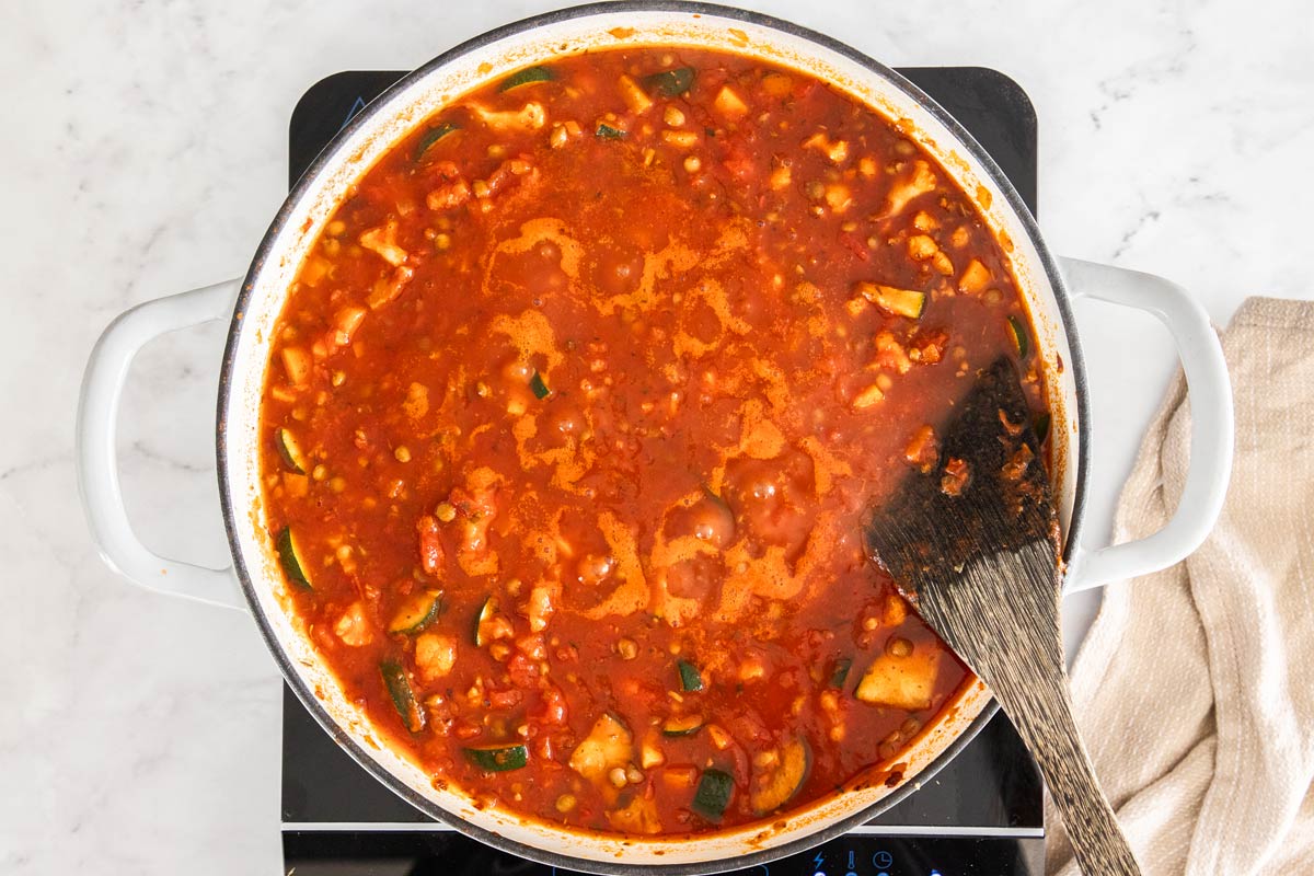 A white ceramic skillet with vegetables, lentils, vegetable broth, and marinara sauce.