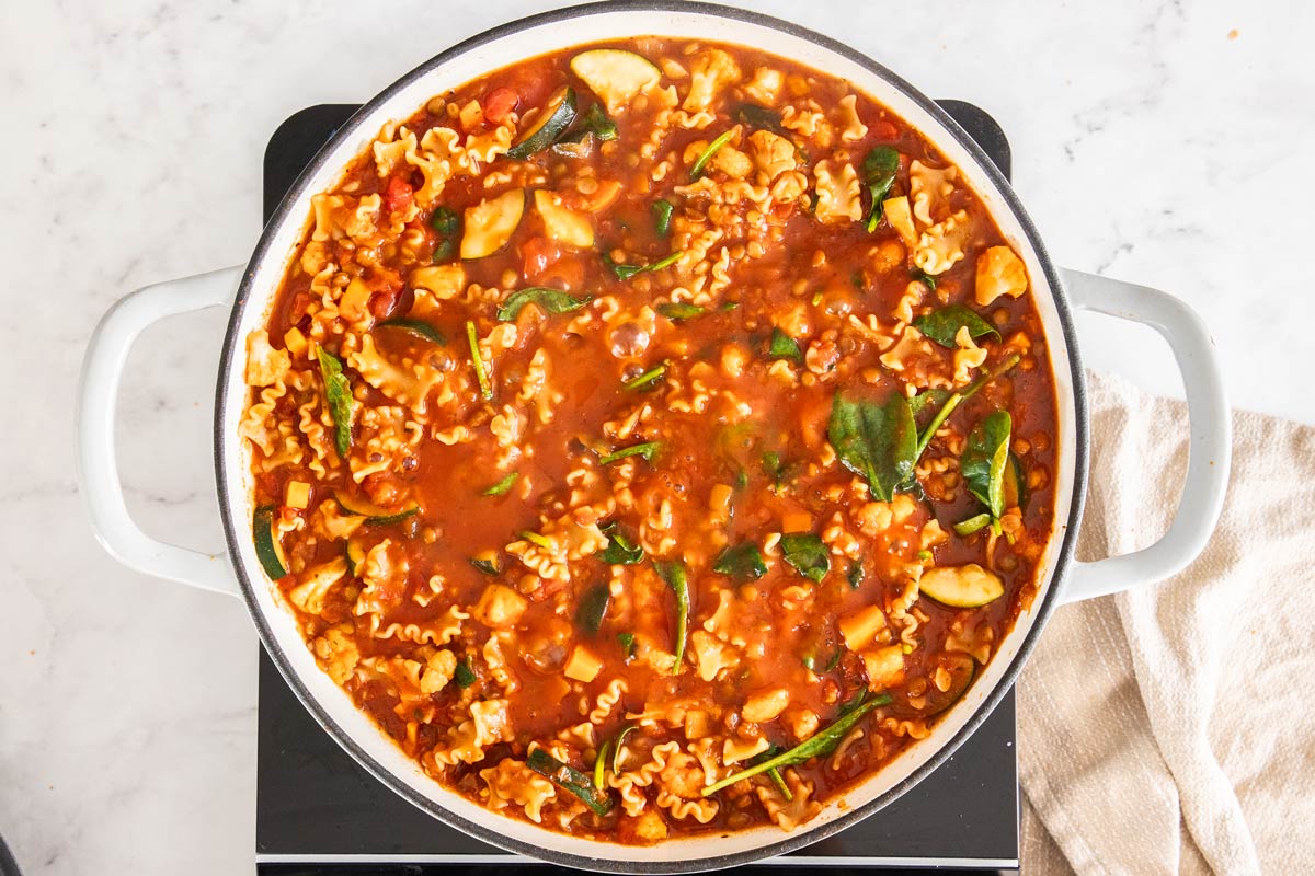 A skillet of vegetables, spinach, and pasta simmering in tomato sauce.
