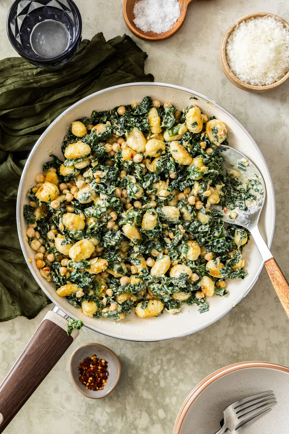 Overhead photo of a pan of creamy gnocchi with chickpeas and kale on a grey surface