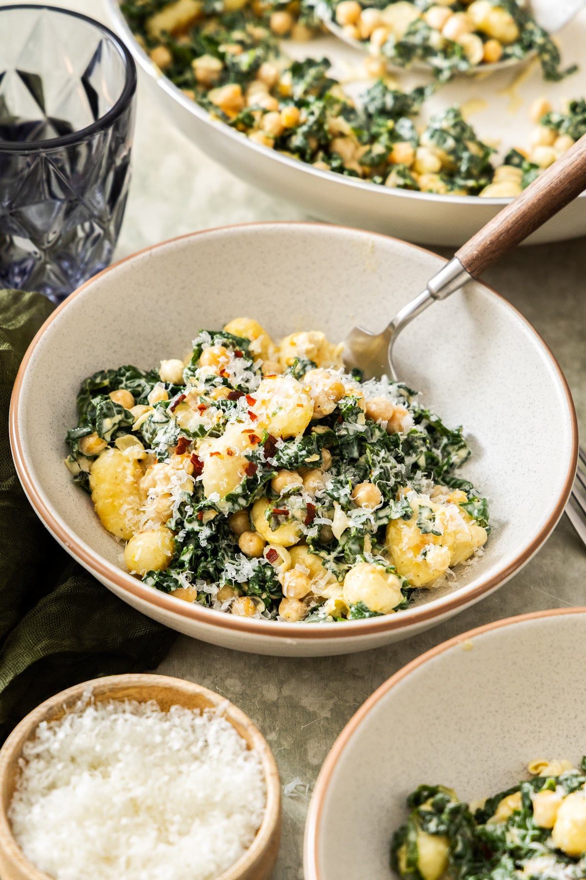 A bowl of creamy gnocchi with chickpeas and kale topped with parmesan.