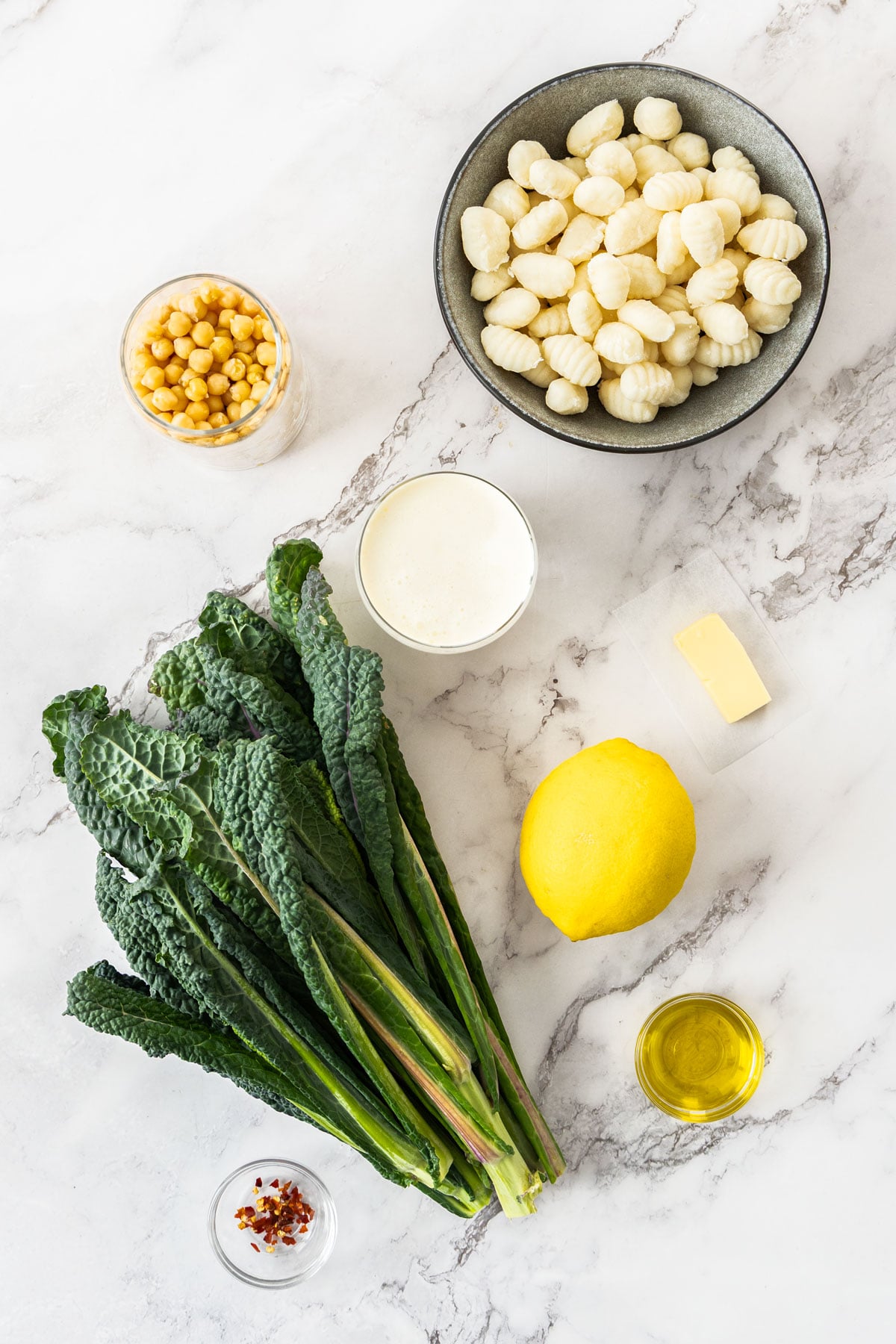 Gnocchi, Tuscan kale, lemon, chickpeas, cream, parmesan, butter, olive oil, and red pepper flakes on a marble background.