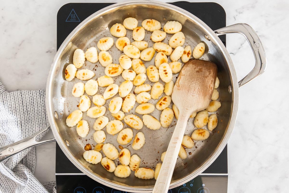 Overhead photo of gnocchi being pan-fried in butter in a stainless steel skillet.