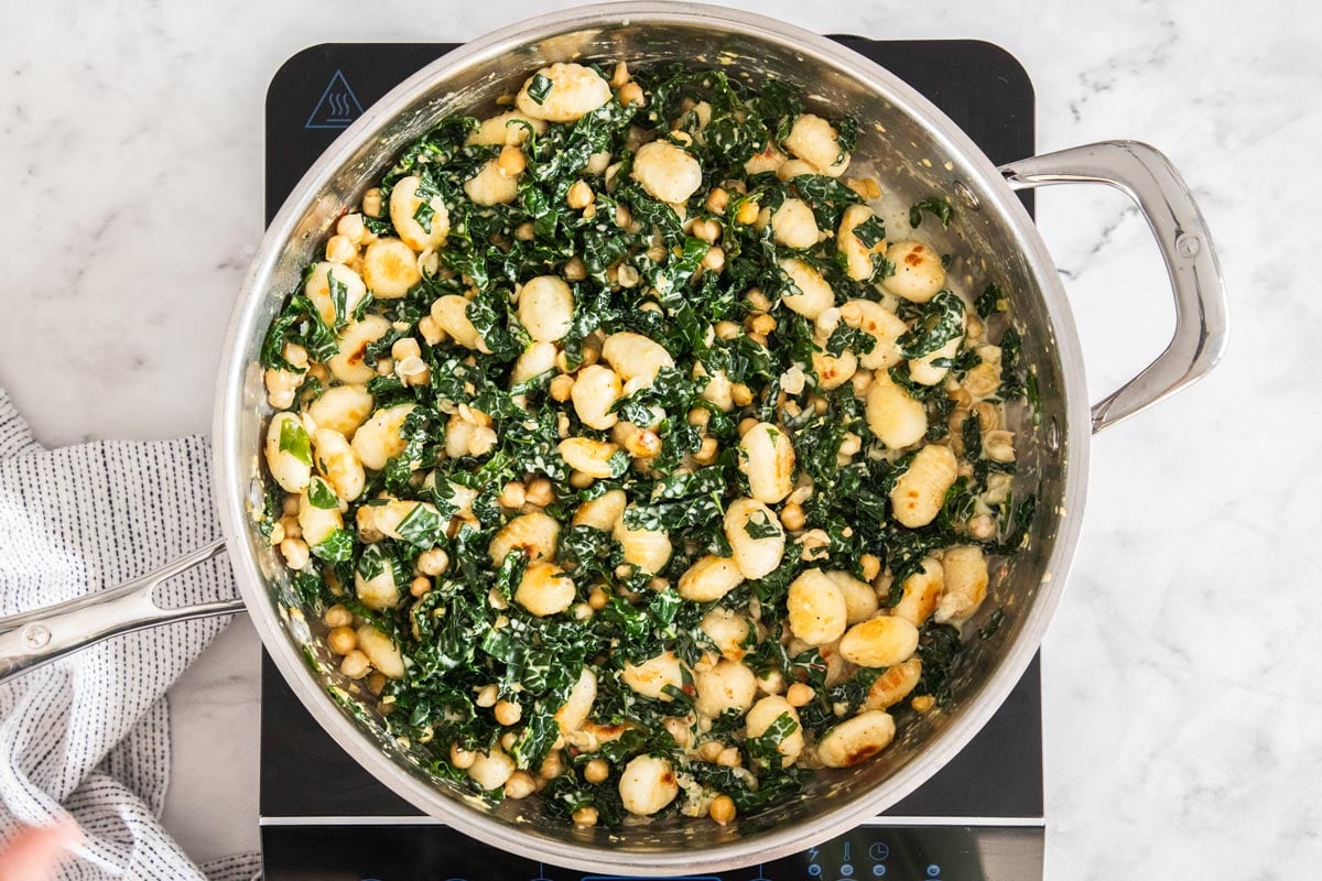 Gnocchi, chickpeas, and kale simmering in a cream sauce in a stainless steel skillet.