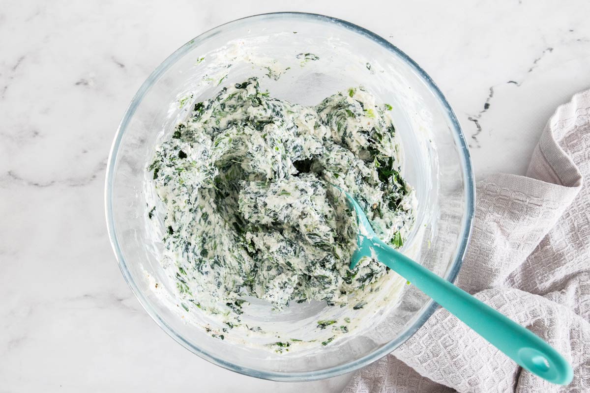 Overhead photo of chopped frozen spinach and ricotta mixed together in a class bowl.