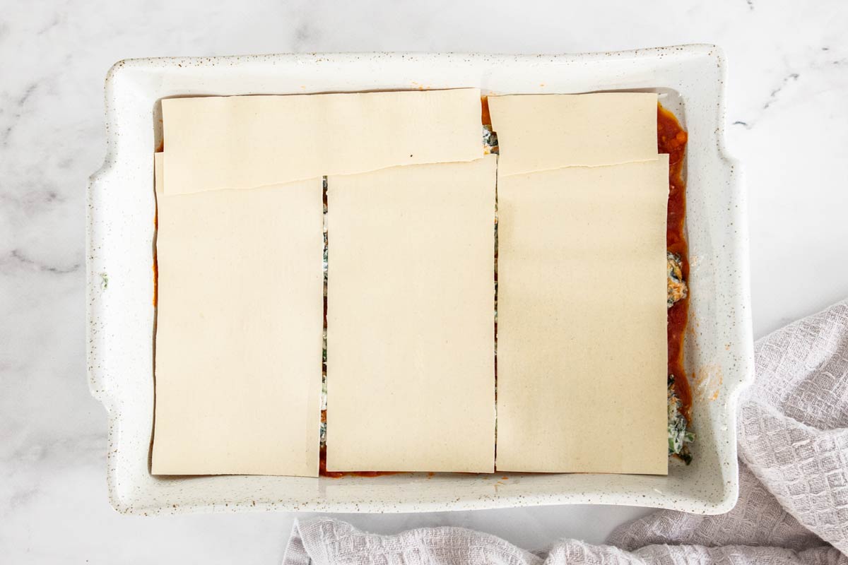 No-boil lasagna noodles placed over spinach and ricotta in a white lasagna pan.