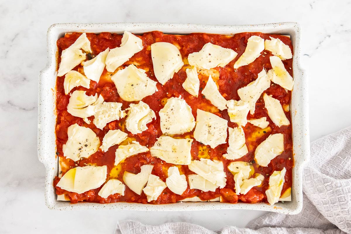 Torn mozzarella on top of a spinach and ricotta lasagna in a white lasagna pan.