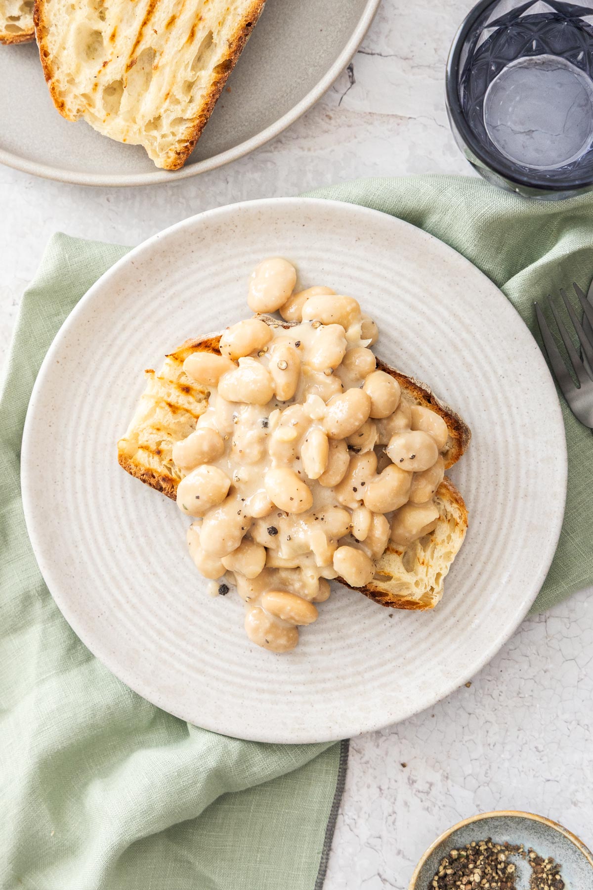 Overhead photo of cacio e pepe white beans on a slice of grilled sourdough toast on a white plate