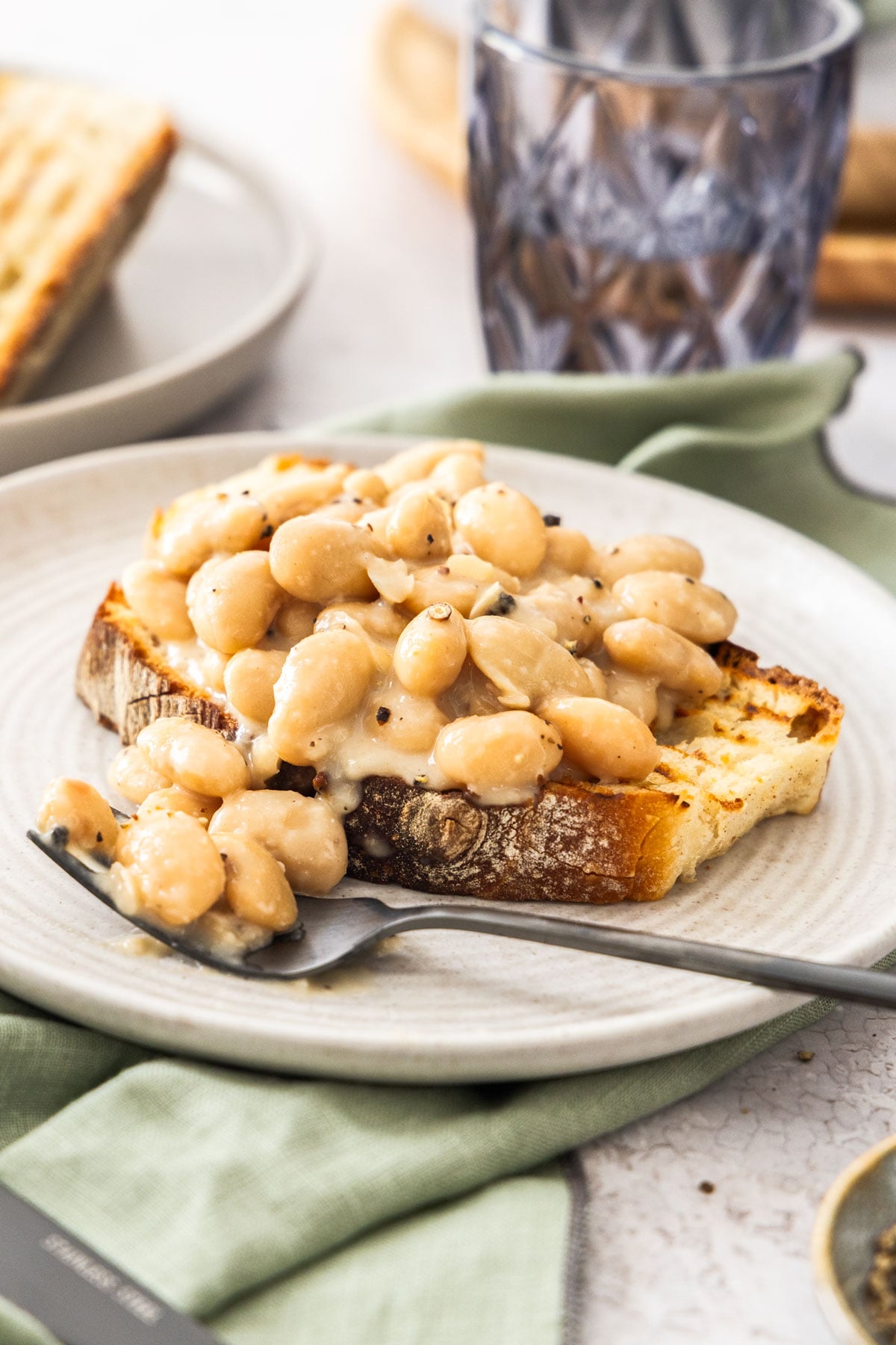 A plate with cacio e pepe beans on a slice of toasted sourdough with a fork to the side