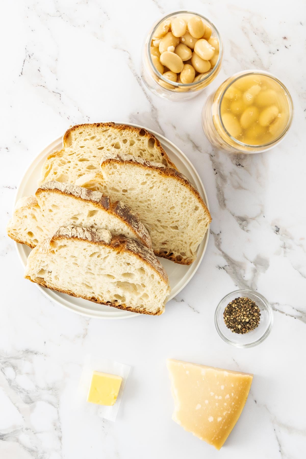Butter beans, sourdough bread, black pepper, butter, and pecorino romano cheese on a marble background