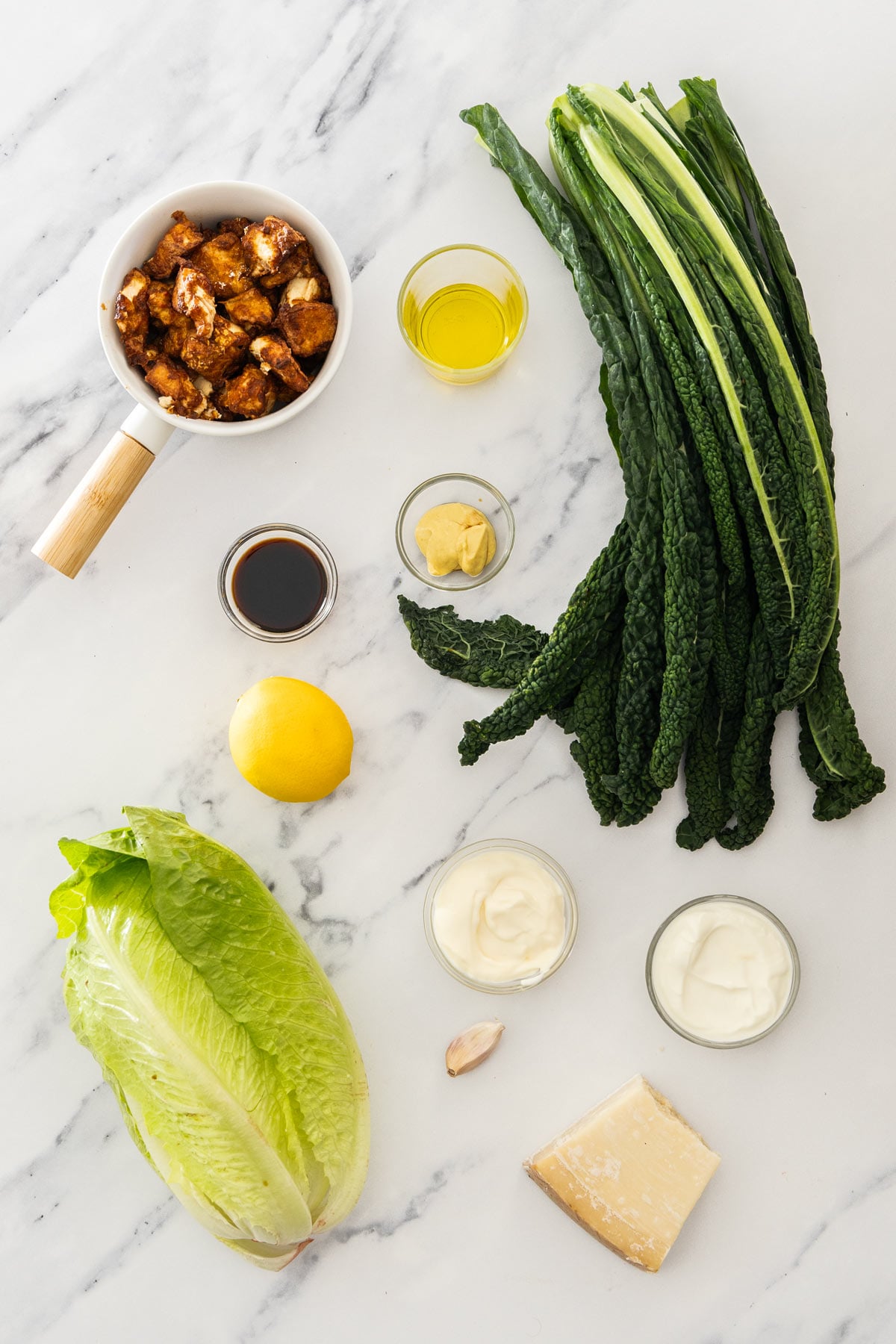 Kale, romaine, parmesan, yogurt, mayo, lemon, dijon mustard, soy sauce, olive oil, garlic, and crispy tofu on a marble background.