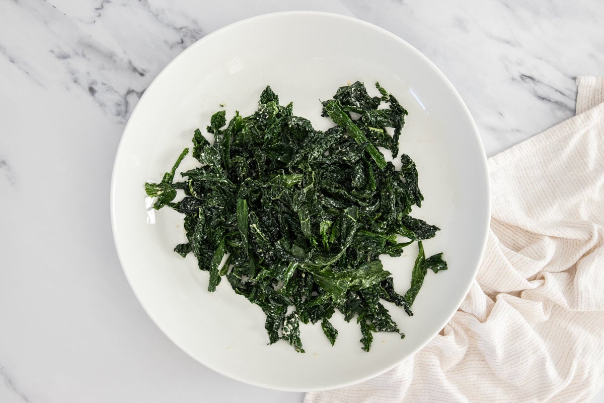 Overhead photo of tuscan kale massaged with caesar dressing in a white salad bowl