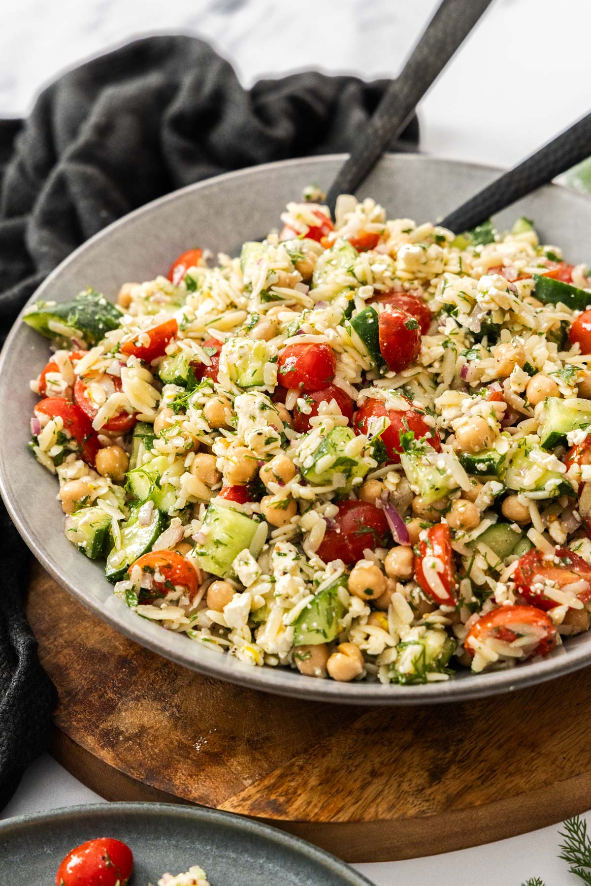 Lemon orzo pasta salad in a large white serving bowl with salad tongs on the side.