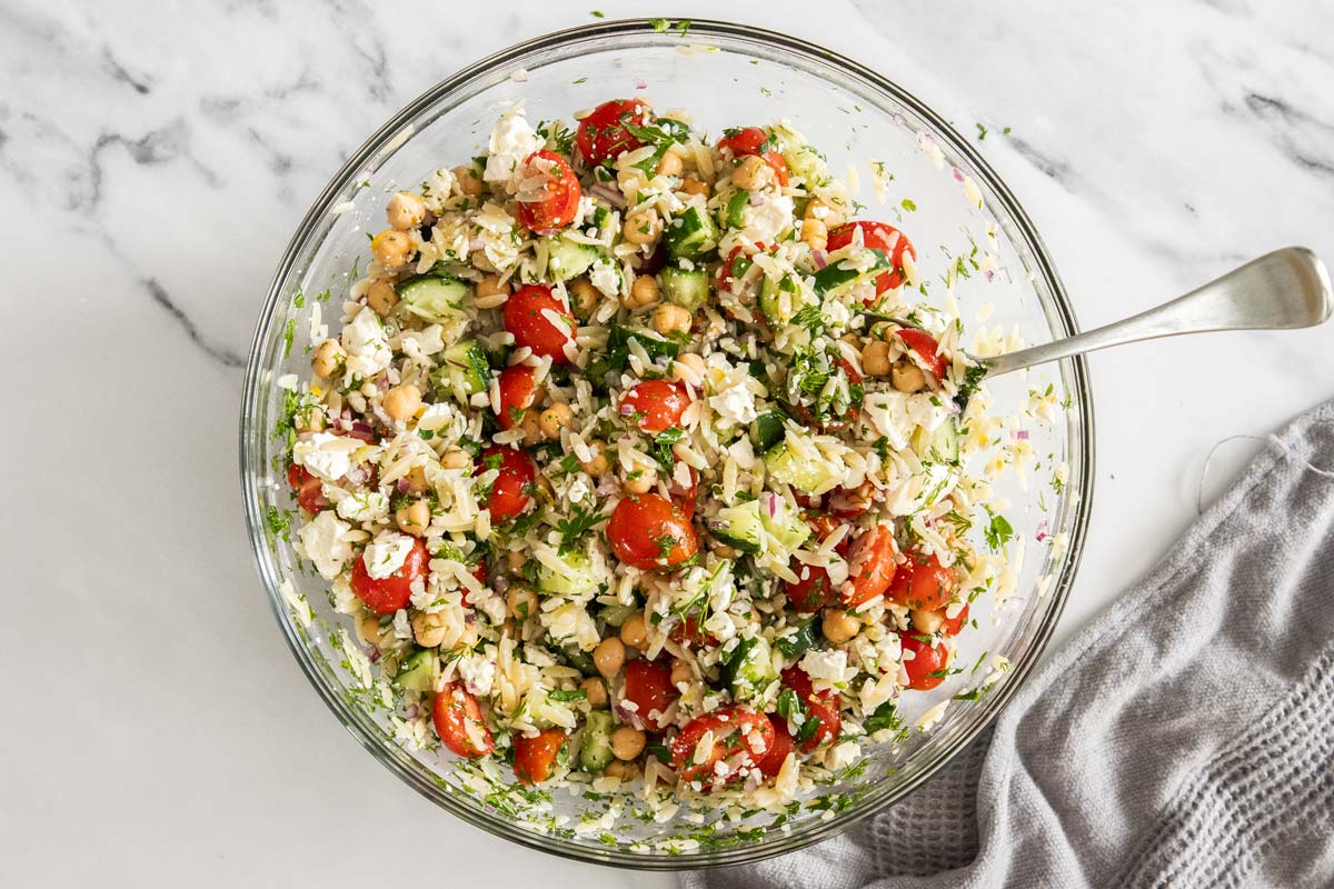 Lemon orzo pasta salad being mixed together in a glass bowl