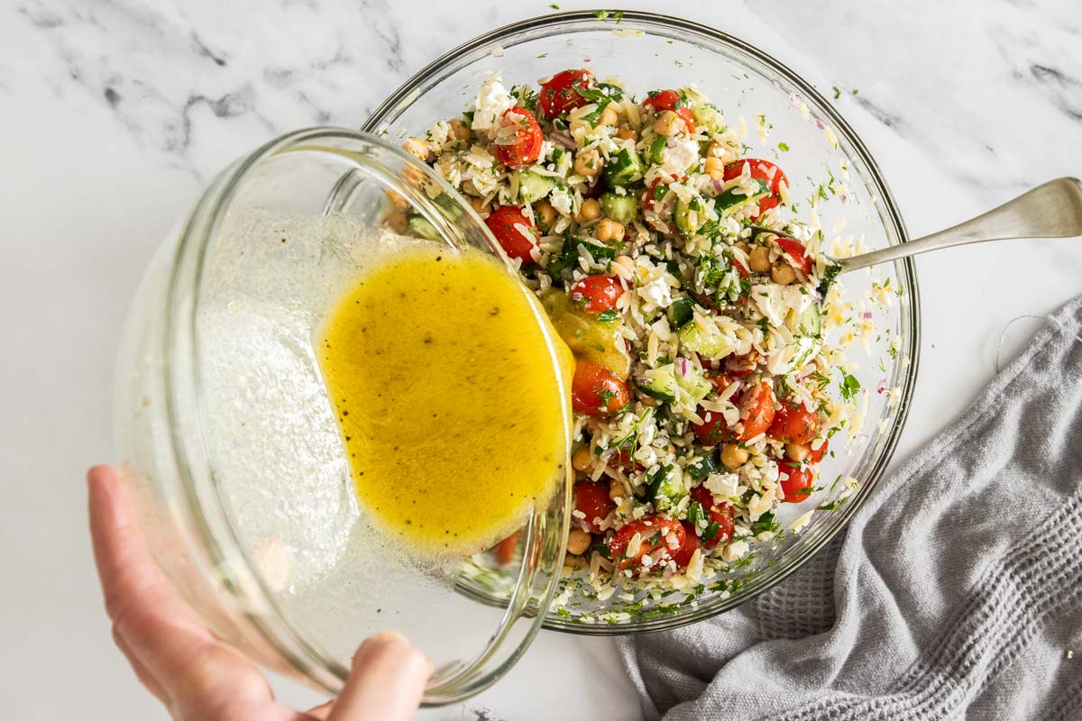 Honey dijon dressing being poured over a bowl of lemon orzo pasta salad