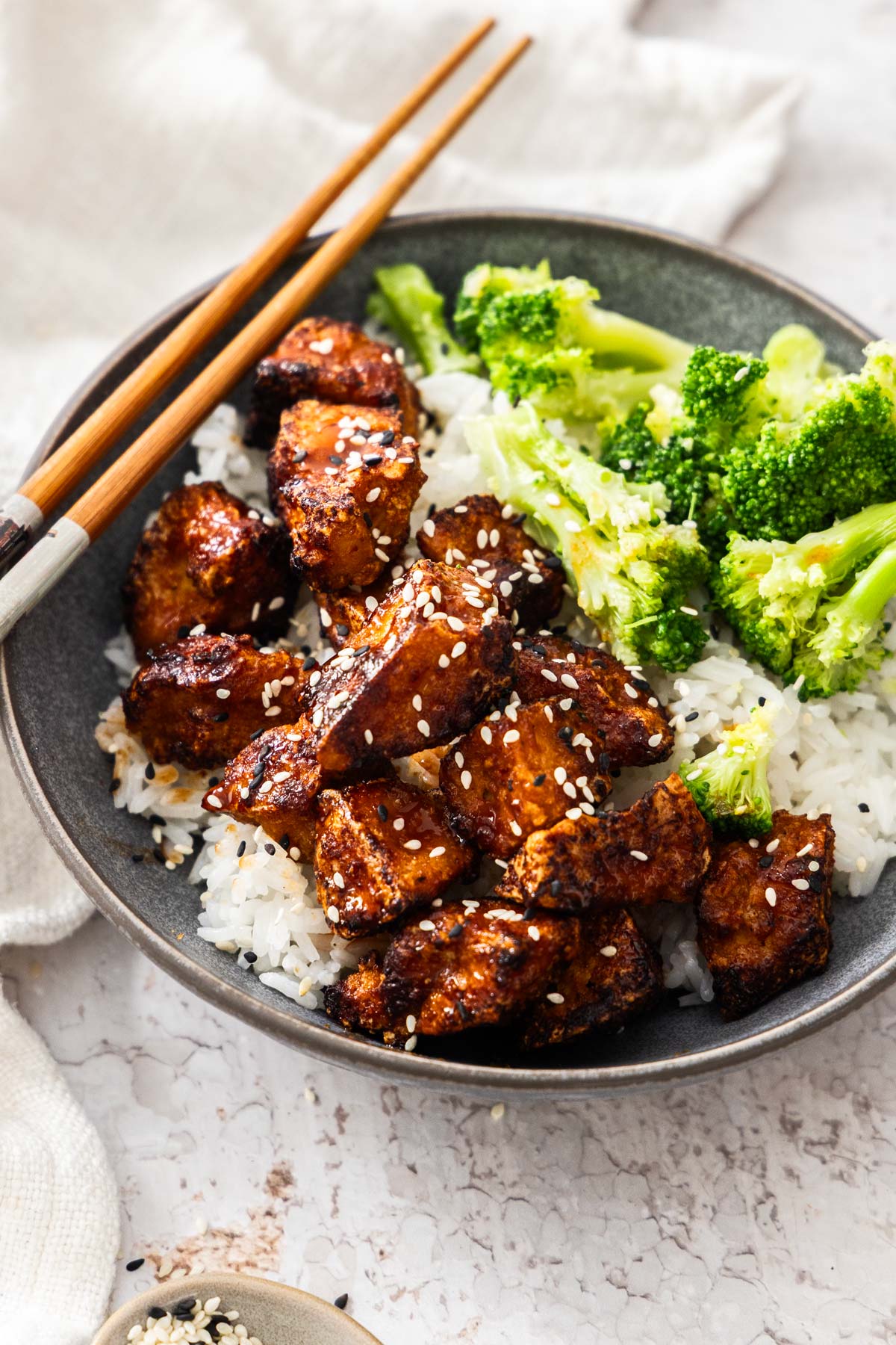 A bowl of sticky gochujang tofu over rice with broccoli to the side
