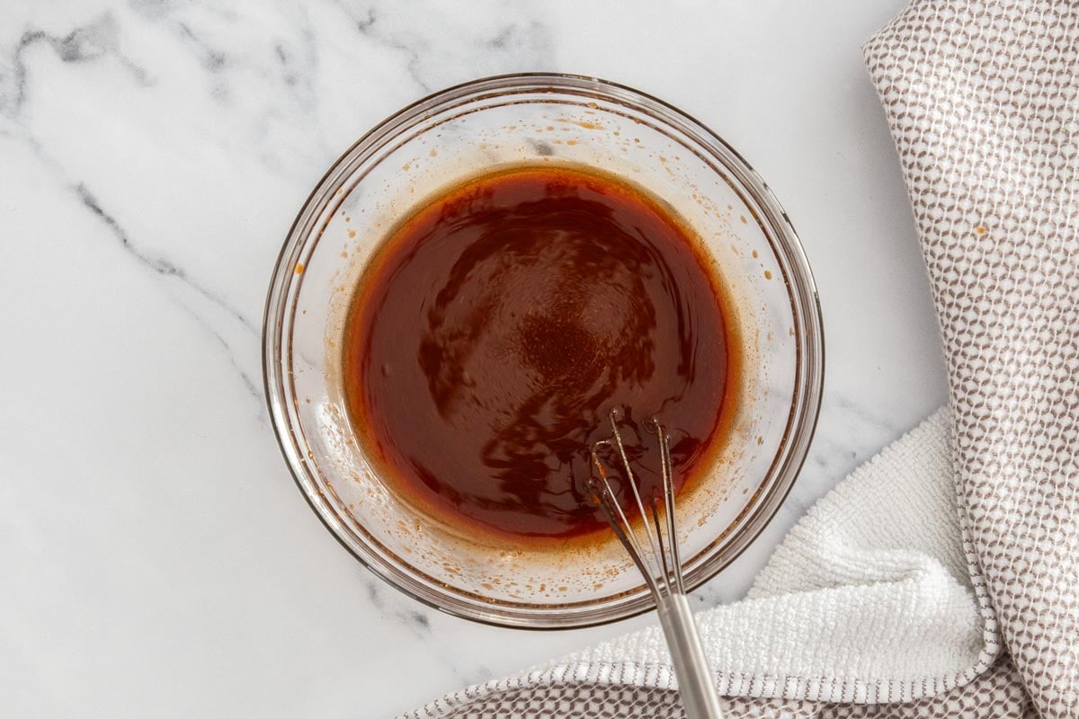 Sticky gochujang sauce being stirred together in a glass bowl.