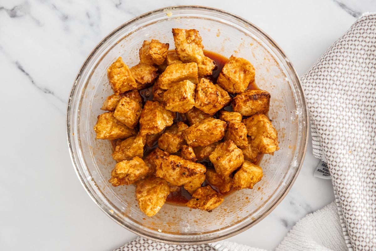 Crispy tofu pieces coated in gochujang sauce in a glass bowl.